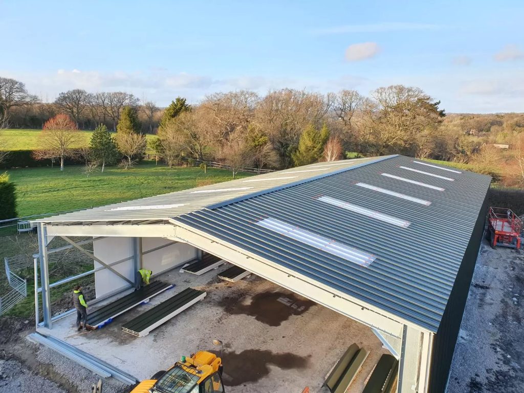 Steel farm building under construction with roof sheets and rooflights going on