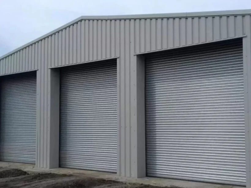 A grey steel storage building with three roller shutter doors that has been designed and installed by Hamilton Steel.