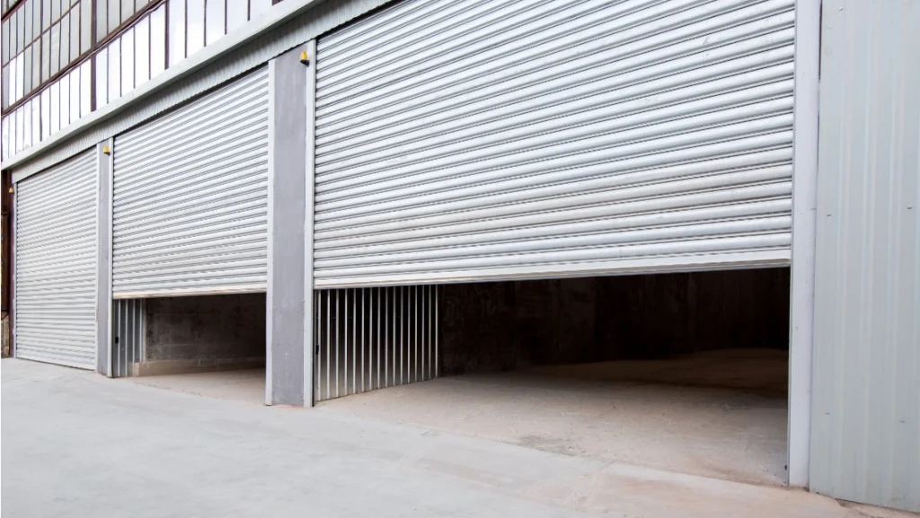 A double set of industrial roller shutter doors open at a large, grey warehouse facility.
