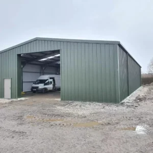 Green agricultural steel building with the doors open and a white van parked inside.