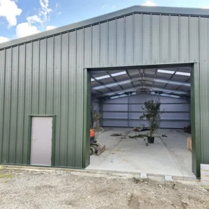 Green agricultural steel building with the doors open and a plant inside.
