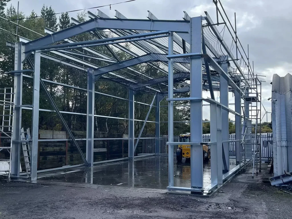 Partially constructed steel frame building with exposed beams and columns, surrounded by scaffolding.