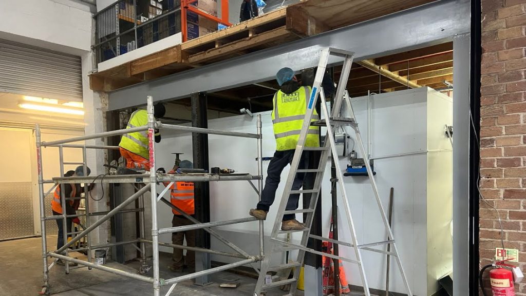 Hamilton Steel Buildings team installing a structural steel goalpost frame beneath an existing mezzanine floor