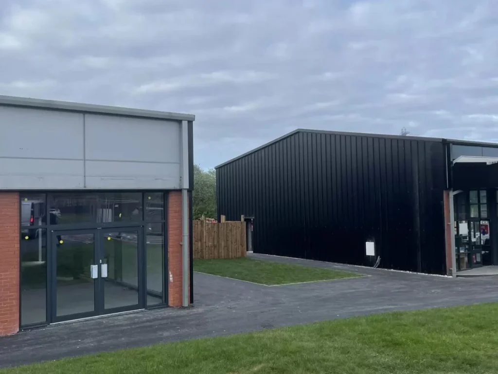 Black clad steel building alongside the glazed retail unit at the Starbucks and Greggs drive through