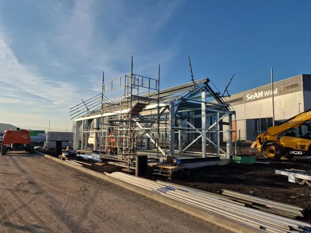 Teesworks HV building steel frame with scaffold edge protection in front of the SeAH Wind facility