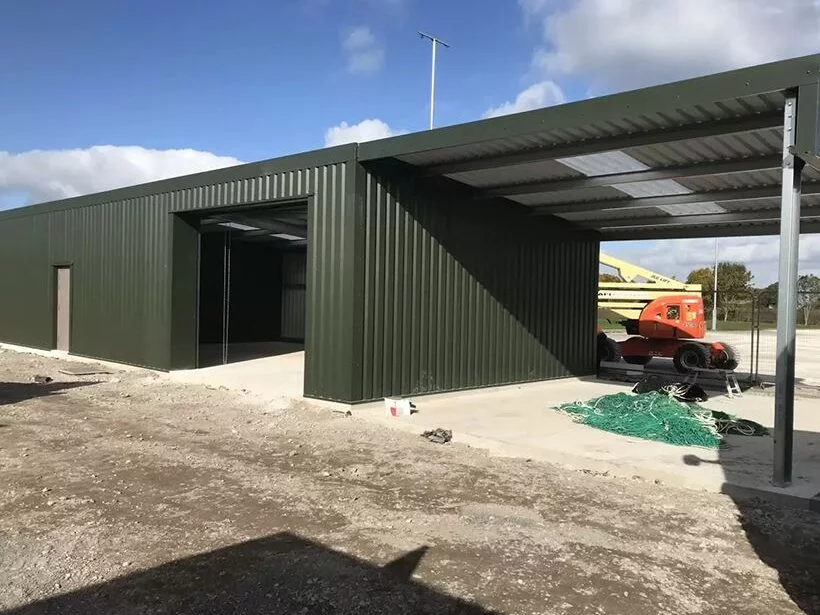 Green clad steel building with open canopy bay under construction at the Welsh Football Association site