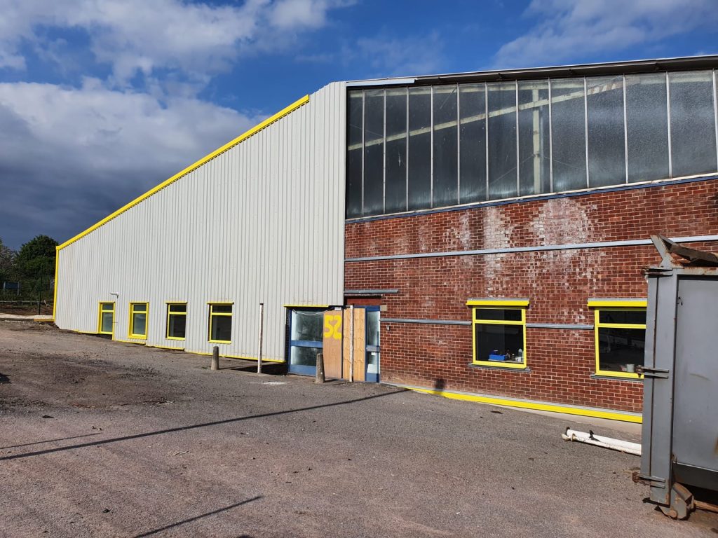 Steel building refurbishment in progress showing yellow-trimmed cladding and repaired brick elevation
