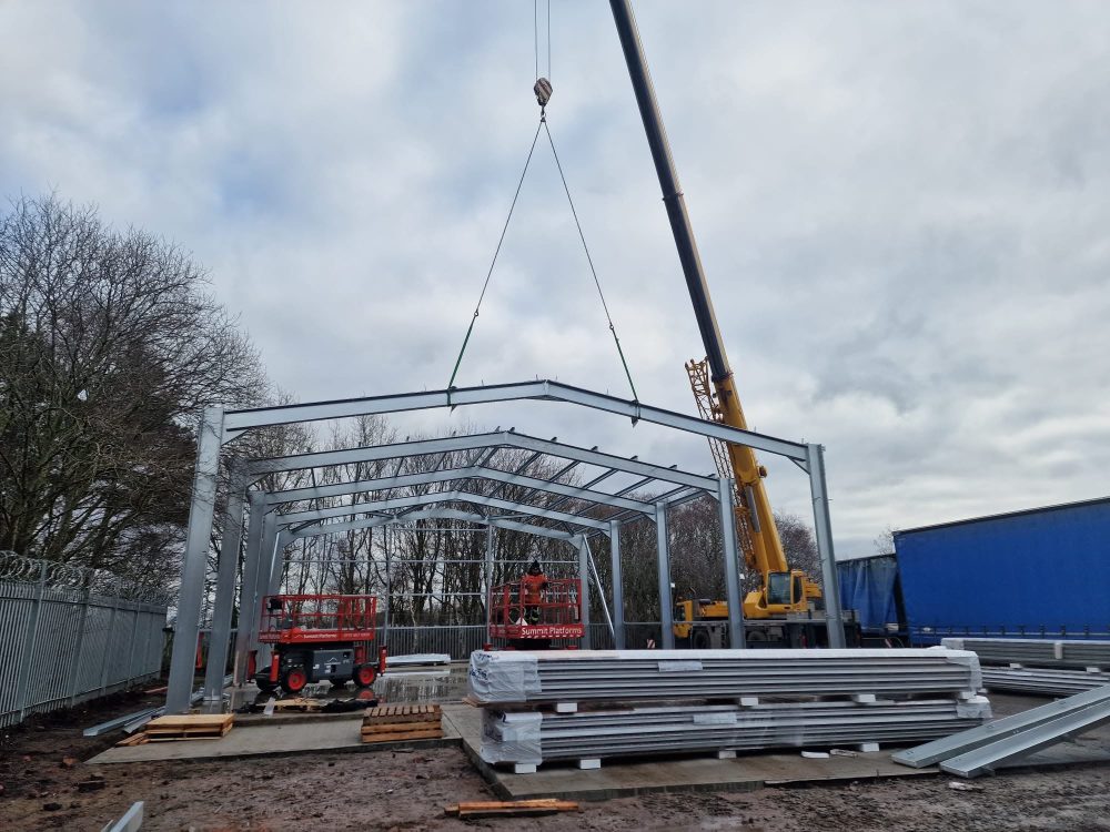 A structural overview of an industrial steel building frame under construction on-site, demonstrating the erection process of steel columns and rafters.