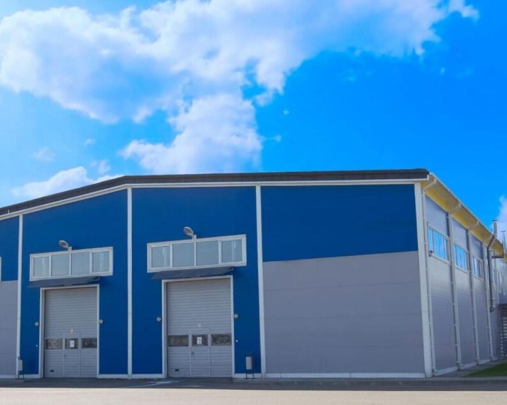 Photograph of large blue commercial steel building with green lawn in the foreground and a blue sky in the background