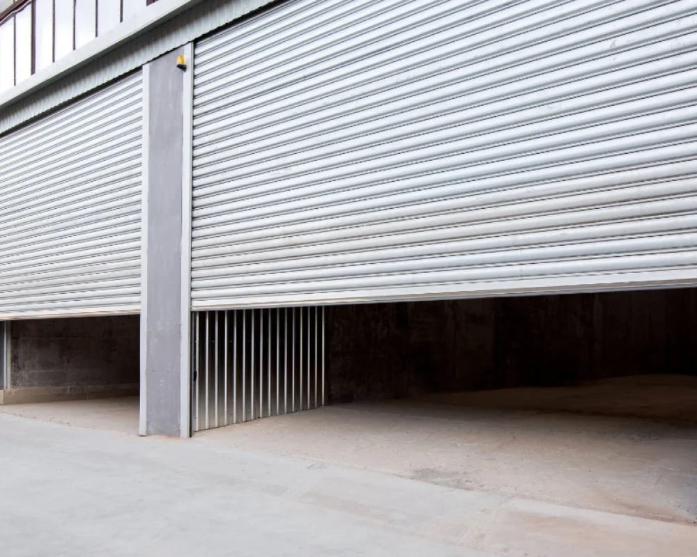 A double set of industrial roller shutter doors open at a large, grey warehouse facility.