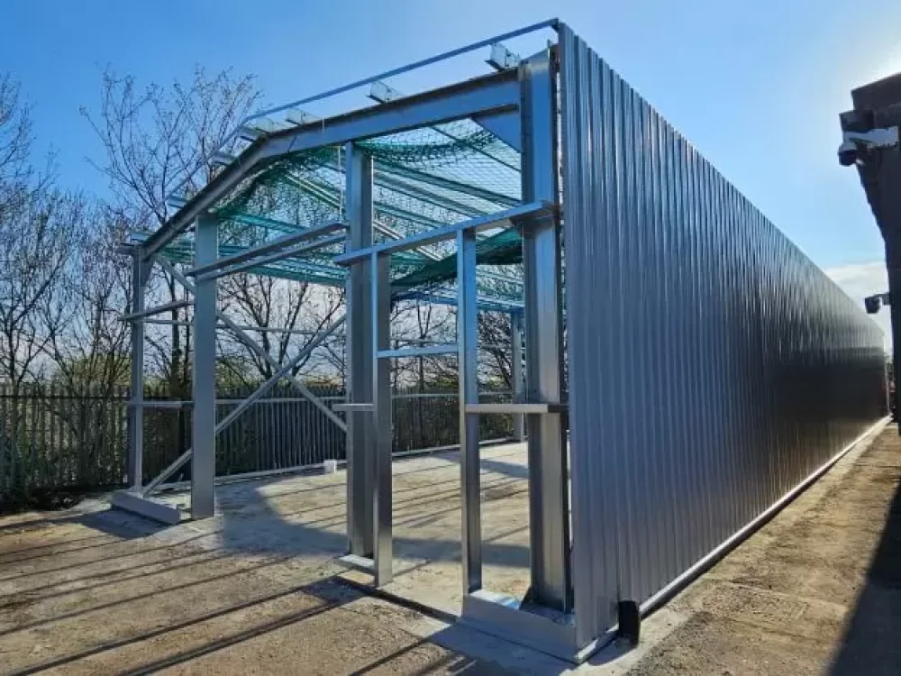 Galvanised steel frame under construction with safety netting, dark green cladding fitted to one side
