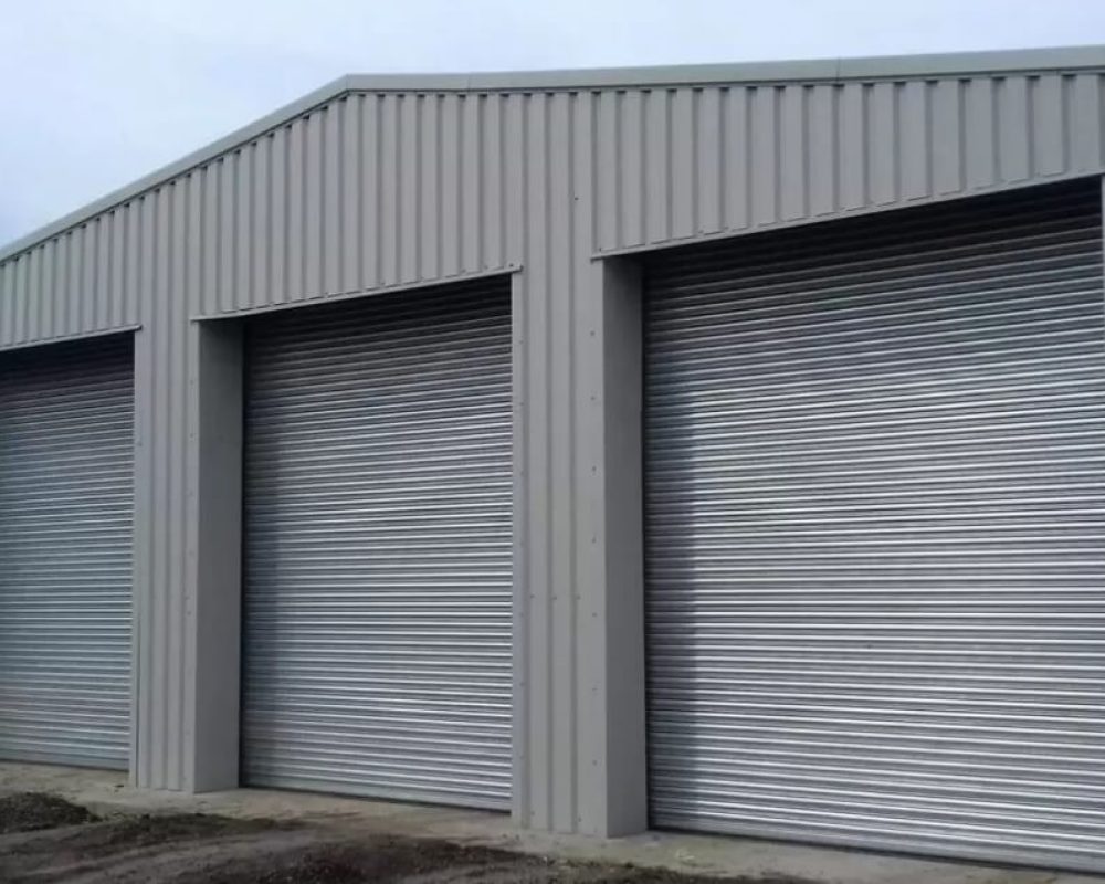 A grey steel storage building with three roller shutter doors that has been designed and installed by Hamilton Steel.