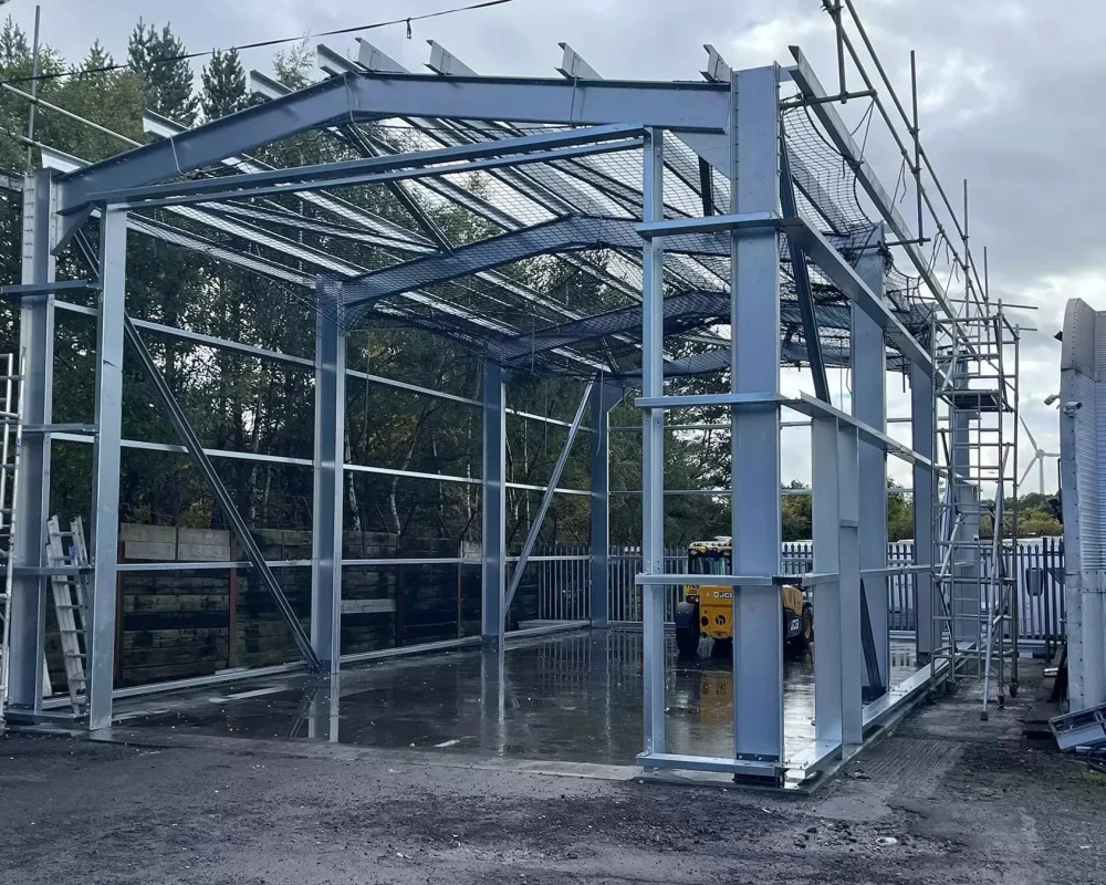 Partially constructed steel frame building with exposed beams and columns, surrounded by scaffolding.