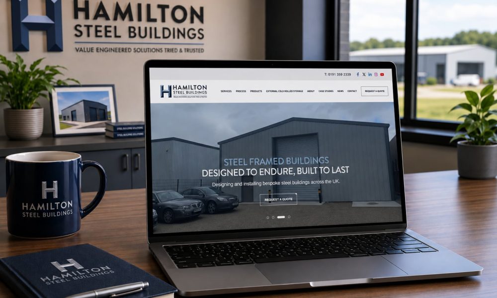 Hamilton Steel Buildings website displayed on a laptop alongside branded mug and notebook in the office