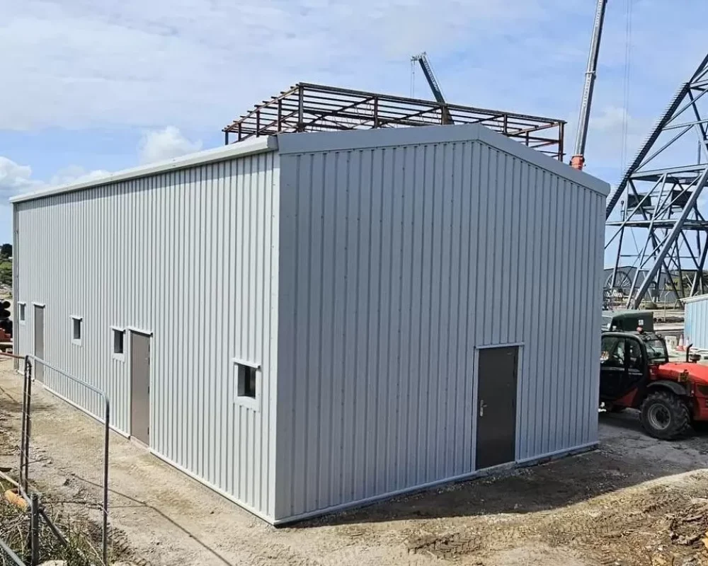 Grey clad steel building at South Crofty Mine with the mine headframe and further steelwork behind