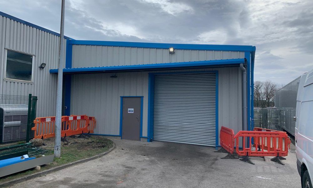 Steel building entrance canopy sheltering a roller shutter door and access door