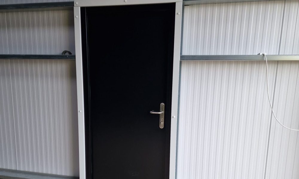 Black personnel access door fitted into white steel building cladding