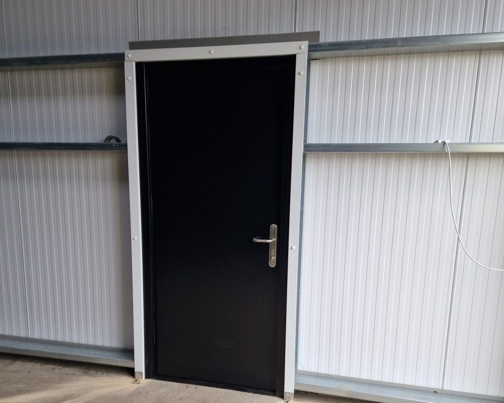 Black personnel access door fitted into white steel building cladding