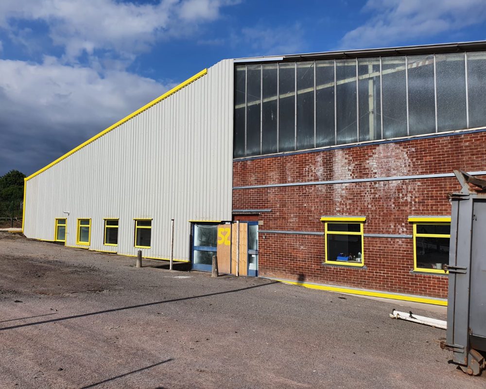 Steel building refurbishment in progress showing yellow-trimmed cladding and repaired brick elevation