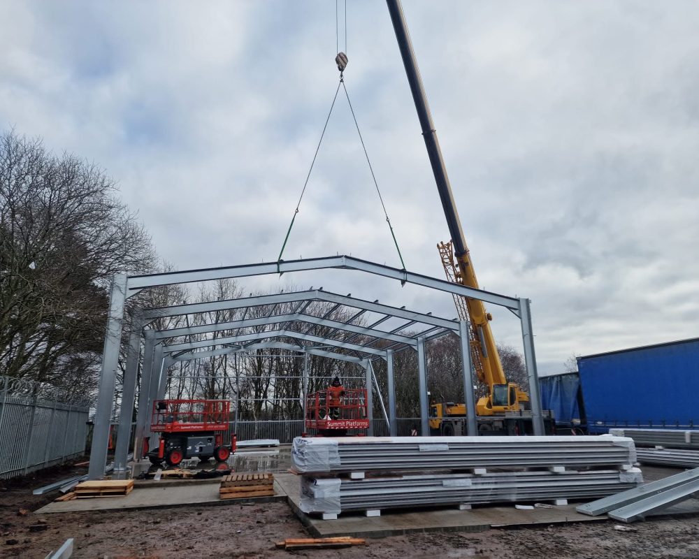 Steel building frame being lifted into place by crane during installation