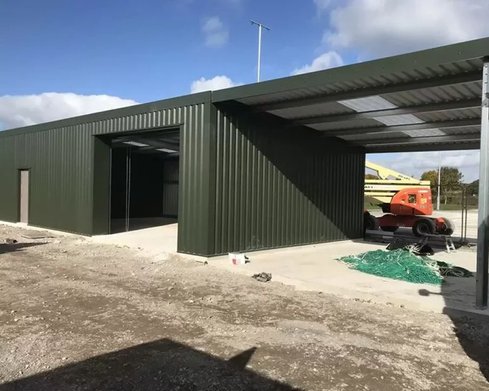 Green clad steel building with open canopy bay under construction at the Welsh Football Association site